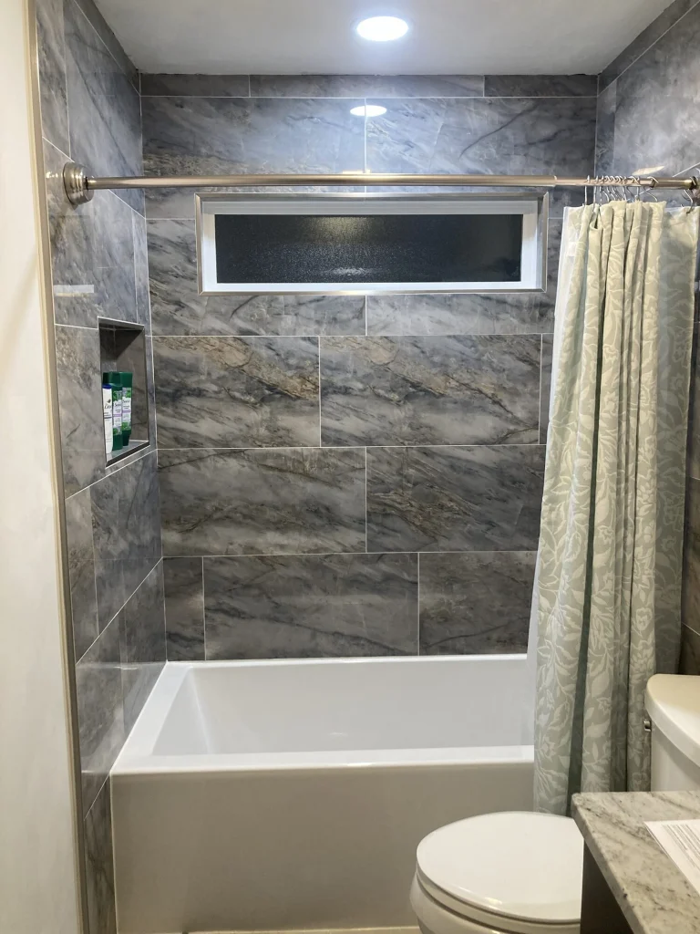 A bathtub surround in large blue-gray marble-look tile, with a window and a recessed niche