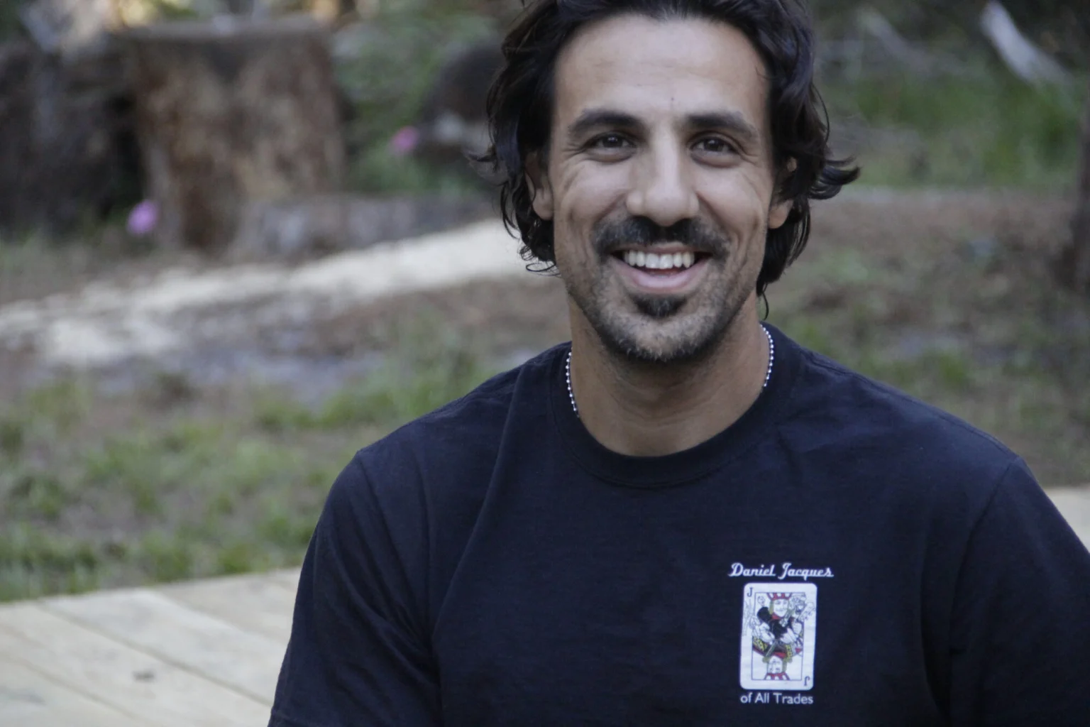 Daniel Jacques, smiling, in a navy Daniel Jacques of All Trades T-shirt