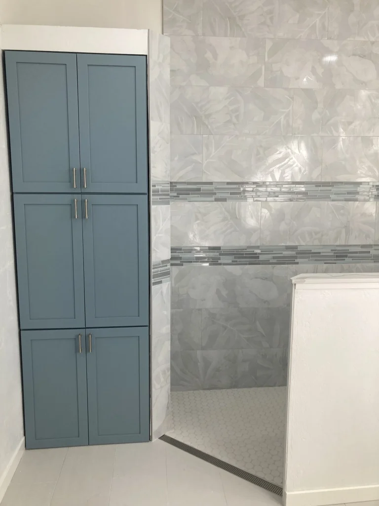 A tall blue linen cabinet beside a curbless shower with a linear drain