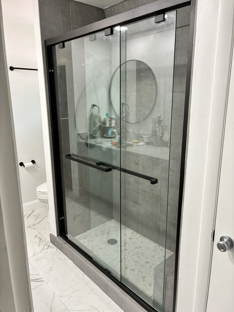 A walk-in shower with black-framed sliding glass doors, gray tile walls and a hexagon tile floor