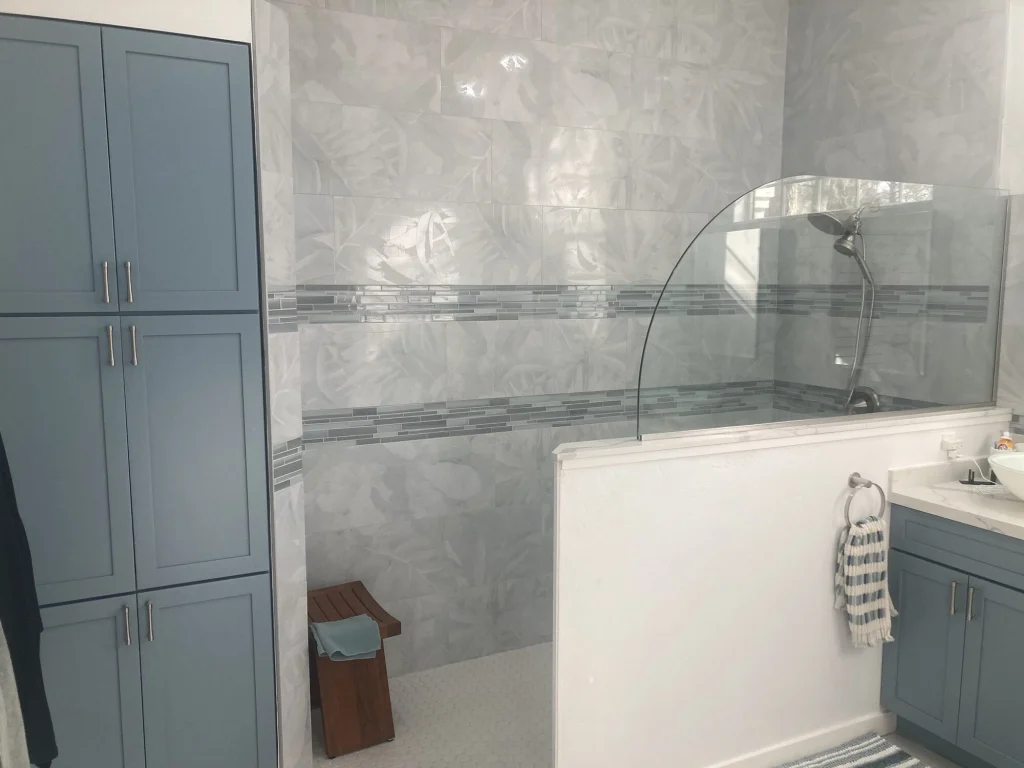 A walk-in shower with leaf-pattern wall tile, glass mosaic bands and a curved glass panel